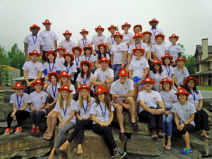 Group of people wearing white shirts and orange hard hats sitting and standing on stone steps outdoors.