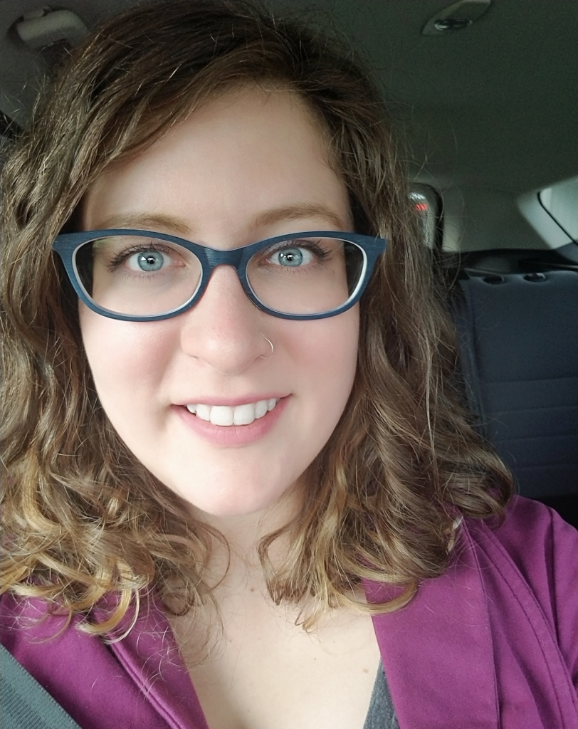 Woman with curly hair and glasses smiling in a car.