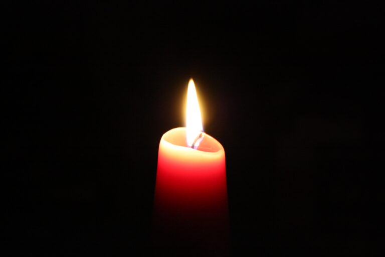 A single red candle burning brightly in a dark room.