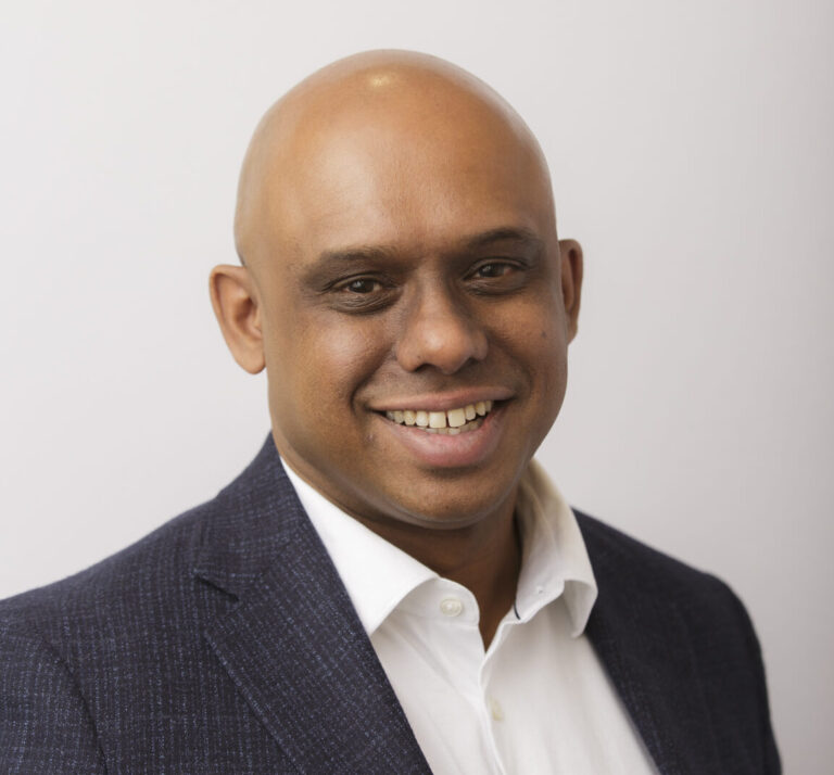 Smiling bald man in a dark blazer and white shirt against a light background.