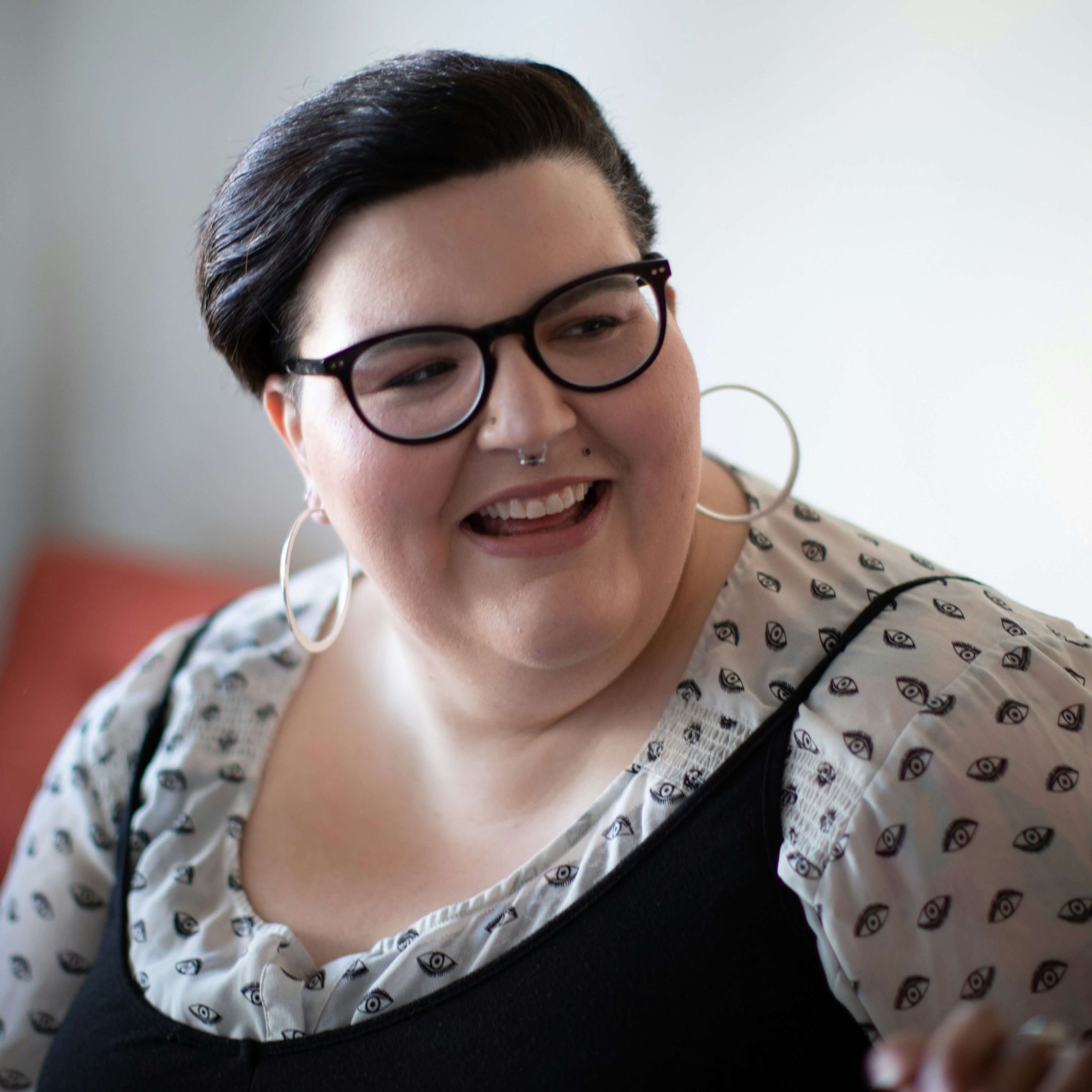 A closeup of a woman with short dark har, glasses, large hoop earrings. She is smiling and looking outside the frame