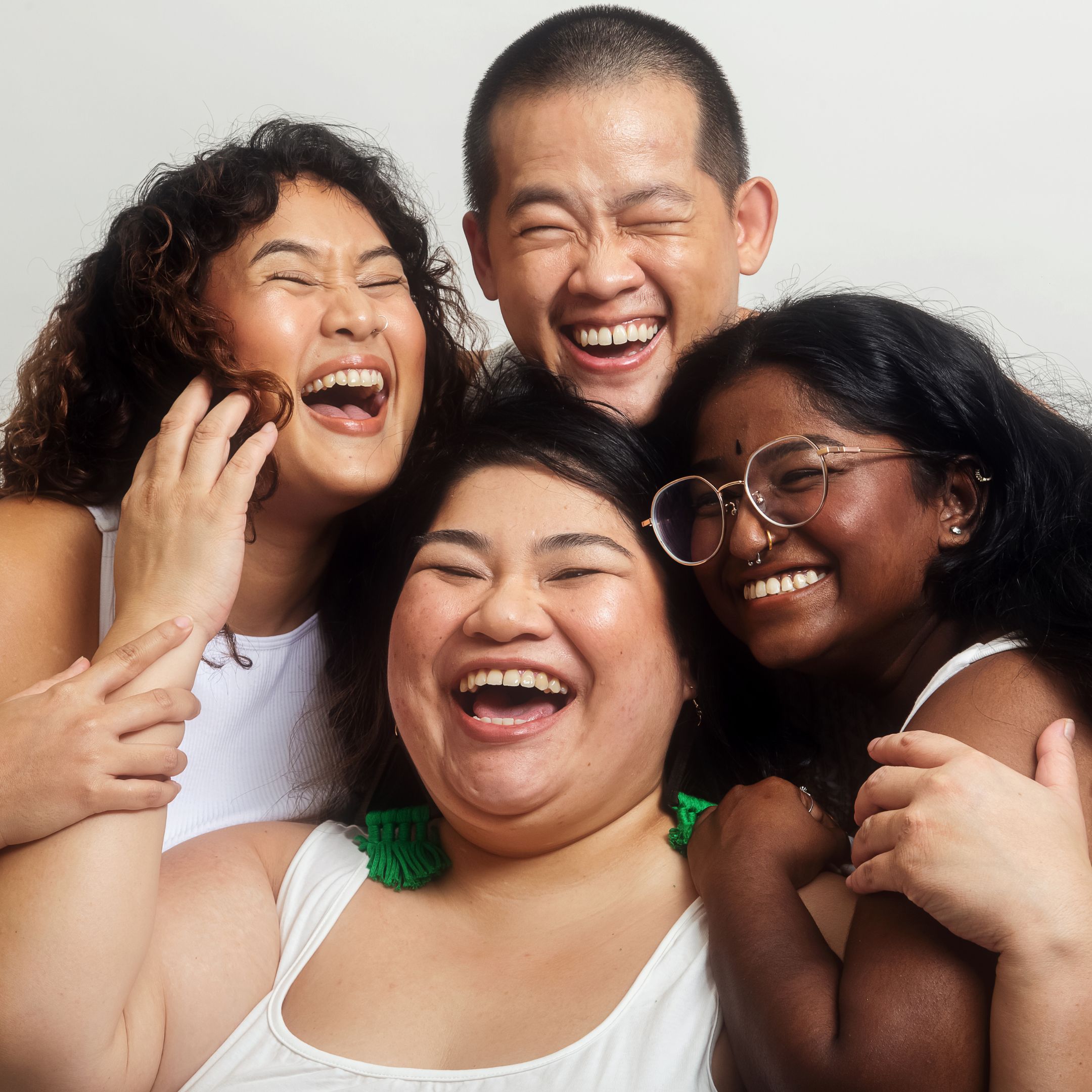 A diverse group of friends pose close together. They are smiling and laughing