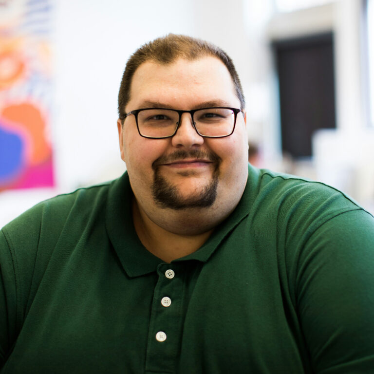 A man living with obesity is wearing glasses and a green golf shirt. He is smiling at the camera.