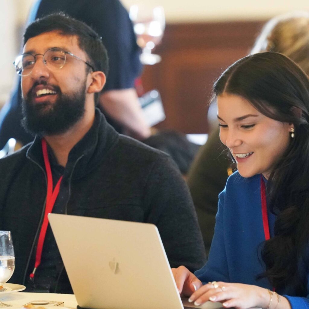 A man with a beard and a woman with dark hair sit at a table. They are in a workshop learning