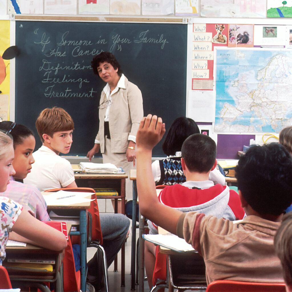 A classroom of elementary school aged children with a teacher standing at the chalkboard.