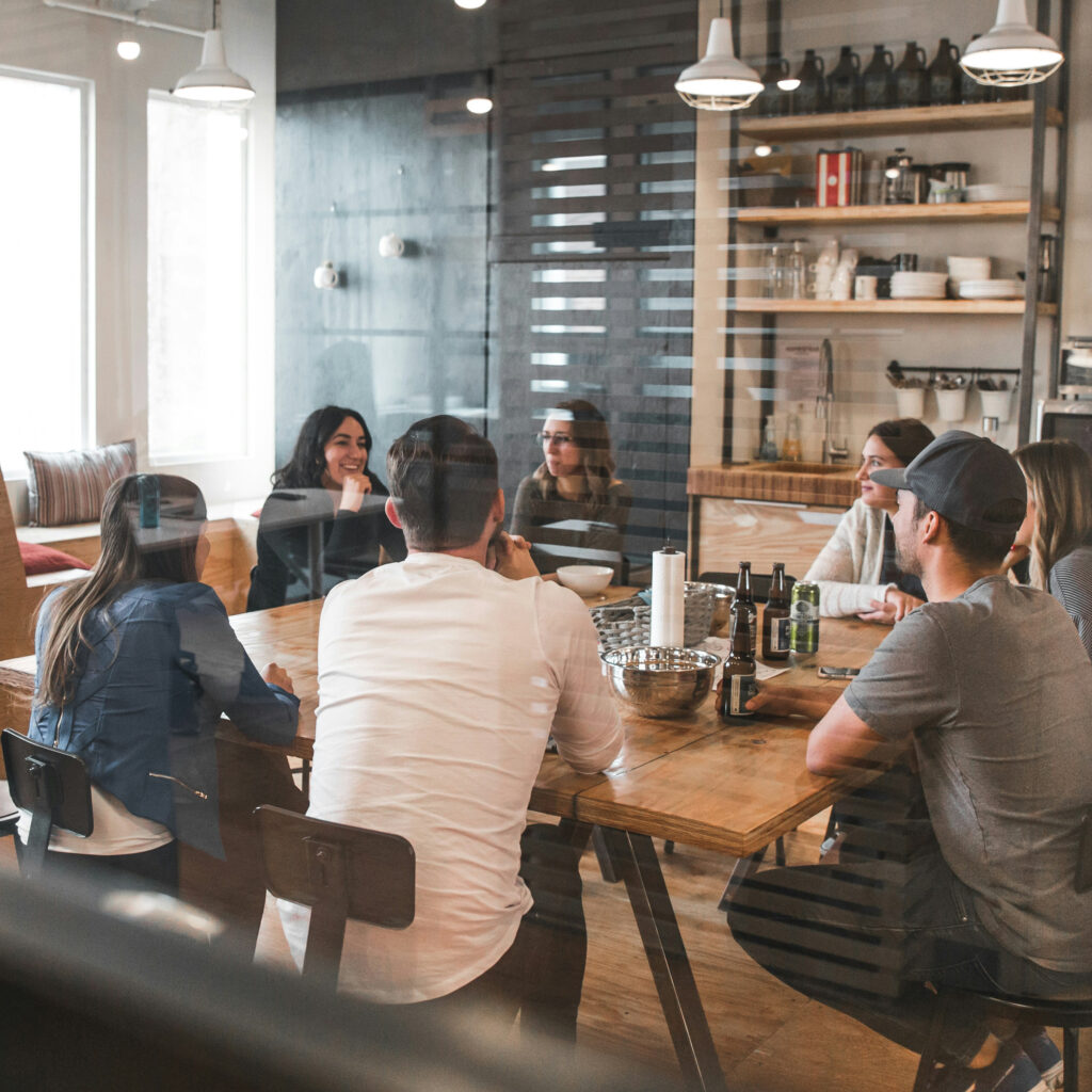 a group of adults sitting around a table in a conference room behind a glass wall.