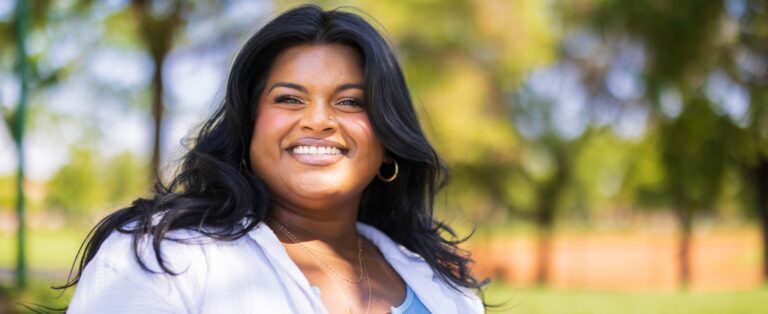 a woman with dark hair standing in a park smiling at the camera