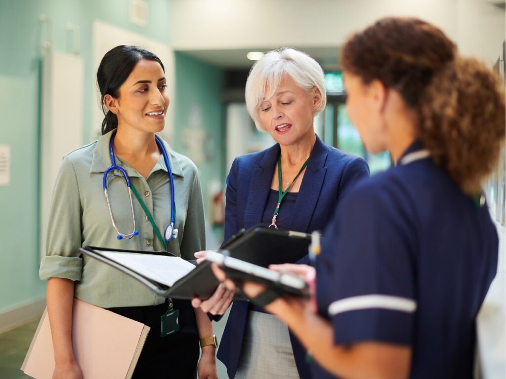 Three healthcare professionals reviewing patient files together in a hospital hallway.