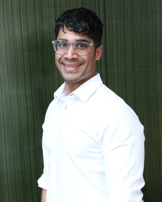 Dr. Roshan Abraham, Lead Author of the 2027 Canadian Adult Obesity Clinical Practice Guideline, stands against a green background wearing a white dress shirt and glasses.