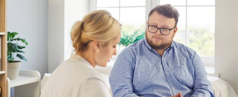 Healthcare professional speaking with a man living with obesity during a medical appointment.