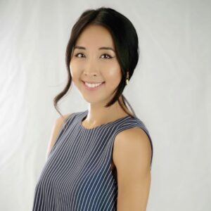 Portrait of Dr. Lisa Ma smiling at the camera, wearing a sleeveless blue-and-white striped top against a light neutral background.